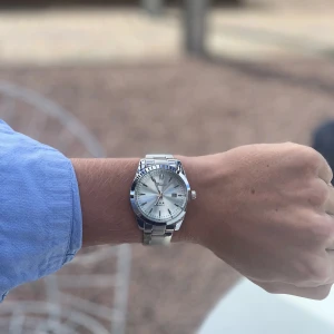 Silverfärgad klocka från Doventi  - Stilren klocka från Doventi med blå urtavla och datumvisning. Klockan har ett klassiskt runt boett i silverfärgad metall och matchande länkarmband. Quartz-urverk och tydliga indexmarkeringar gör den både snygg och enkel att läsa av. Finns box och går att justera