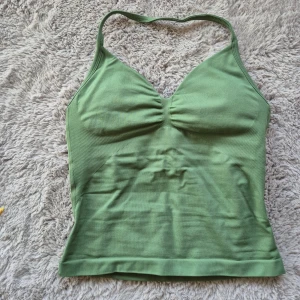 Gtech performance cami halter top - Performance cami halter top från Gtech i färgen Grass Green. Materialet är stetchigt och något tjockare tyg, med öppen rygg och urringad vaderad byst. Linnet är använt en gång så skicket är som nytt. Storlek S. 90% nylon, 10% spandex. 