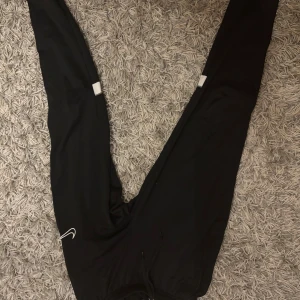 Svarta Nike Dri-Fit träningsbyxor S - Svarta träningsbyxor från Nike med Dri-Fit-teknologi, perfekt för dig som gillar att röra på dig. Byxorna har en slim passform, snörning i midjan och diskret Nike-logga på benet. Materialet är syntet och känns lätt och smidigt.