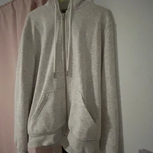 Ljusgrå zip hoodie med huva - Ljusgrå hoodie med dragkedja och huva, perfekt för chill dagar. Tröjan har två stora fickor framtill och snörning i huvan. Mjuk och skön i bomullsmix, med ribbade muddar och avslappnad passform. Tröjan är i storlek M men passar även S. 