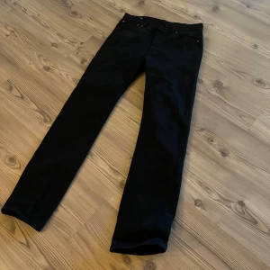 Svarta Levi's 501 jeans, straight fit - Svarta Levi's 501 jeans med klassisk straight fit. Snygga kopparfärgade nitar och ikonisk läderpatch bak. Jeansen har normal passform och är tillverkade i slitstarkt bomullsmaterial. Perfekt för dig som gillar tidlös stil och vill ha ett par jeans som funkar till allt.