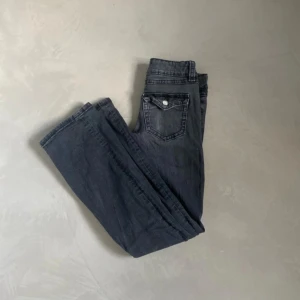 Bootcut svarta jeans med fickdetalj - Snygga svarta jeans med bootcut passform och klassisk femficksdesign. Jeansen har en cool ficka med lock och knapp på baksidan, vilket ger dem en unik touch. Materialet är mjukt denim och färgen är mörk svart med lätt tvättad look.