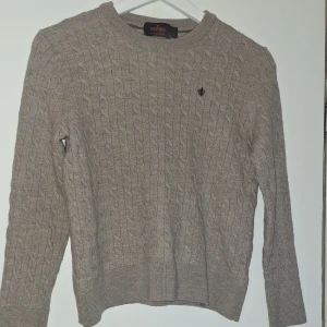 Beige kabelstickad tröja Morris L - Kabelstickad beige tröja från Morris i 100% merinoull. Klassisk rund hals och diskret broderad logga på bröstet. Snygg passform med ribbade muddar vid ärmslut och nederkant. Perfekt för dig som gillar stilrena och tidlösa plagg. Kvaliten är 10/10. Passar folk runt 150cm. Modellen är 162 cm