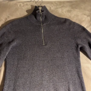 Mörkgrå stickad half zip tröja - Säljer en mörkgrå stickad tröja från Mango med ribbad struktur och half zip-dragkedja i halsen. Tröjan har långärmade ärmar och en hög krage som kan vikas ner. Strl S men passar M.