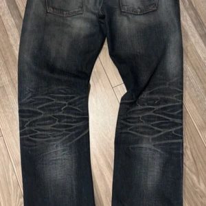Nudie Hank Rey mörka jeans med mönster - Säljer ett par Nudie Hank Rey jeans i mörkblå tvätt med coolt mönster på benen. Jeansen har klassisk femficksdesign, raka ben och orange sömmar. Materialet är slitstarkt denim och passformen är normal med straight leg. Storleken står som 36/34 men är mindre, se mått sista bild