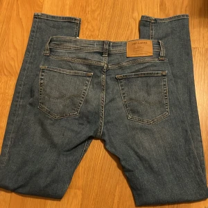 Slim fit jeans från Jack & Jones - Snygga blå jeans från Jack & Jones i modellen Slim Glenn. De har klassisk femficksdesign, smal passform och normal midja. Storlek W29 L32. Jeansen är tillverkade i mjukt denimtyg med lätt tvättad look och subtila slitningar. Perfekta för dig som gillar en modern och stilren stil.