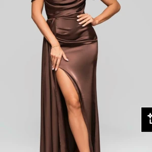Brun långklänning med snörning - Snygg brun långklänning i satinliknande material med offshoulder och smala axelband. Klänningen har en hög slits framtill och snygg snörning i ryggen som ger en extra detalj. Perfekt för dig som vill sticka ut med en elegant och trendig look.