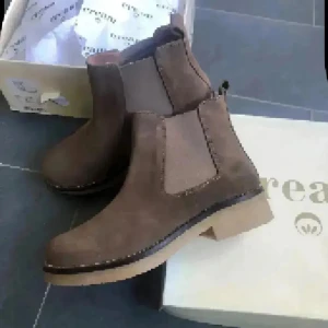 Bruna chelsea boots från Cream mocka skinn nya - Snygga bruna chelsea boots från danska  Cream med rund tå och platt sula. Skorna är tillverkade i mocka och har elastiska paneler på sidorna för enkel påtagning. Perfekt för dig som gillar stilrena och klassiska boots med en modern touch.