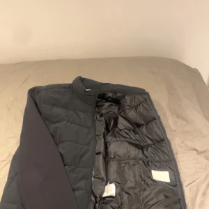 Svart pufferjacka från Zara - Svart pufferjacka från Zara med quiltad framsida och mjuka, långärmade ärmar. Jackan har dragkedja hela vägen och en stilren, enkel design. Materialet är polyester och syntet, perfekt för kyliga dagar. Snygg och clean look som funkar till många stilar.