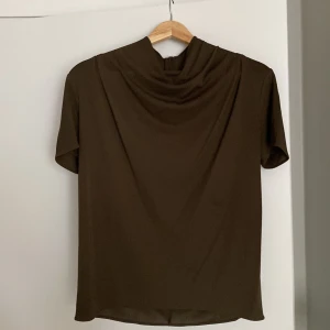 Oliv grön topp med draperad hals - Säljer en suuuper elegant topp med korta ärmar och snyggt draperad hals. Köpt för 2000kr från tiger of sweden och har bara haft på mig den en gång på julafton! Passar mig som vanligtvis har storlek s/m😊🩷