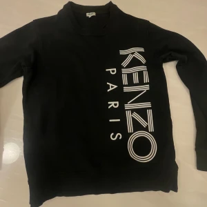 Svart sweatshirt från Kenzo Paris - Svart sweatshirt från Kenzo Paris i storlek L med stort vitt tryck längs framsidan. Tröjan har långärmad design, rund hals och ribbade muddar. Materialet är mjukt och känns som bomull, perfekt för en chill och stilren look.