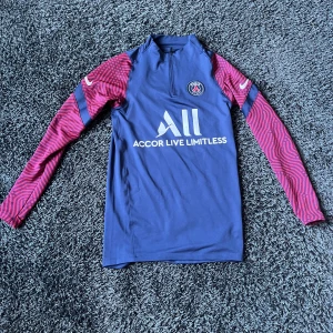 PSG långärmad träningströja Nike - Säljer en snygg PSG långärmad träningströja från Nike med blå kropp och röda, randiga ärmar. Tröjan har halv dragkedja fram, PSG-logga på bröstet och Accor Live Limitless-tryck. Hör av dig gärna om du har några funderingar.