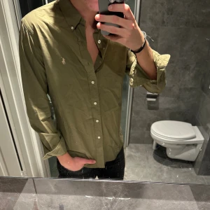 Olivgrön skjorta från Ralph Lauren - Snygg olivgrön skjorta från Ralph Lauren med klassisk button-down krage i skin fit. Jag på bilden är 188cm och bär storlek M. Hör av er vid funderingar:)