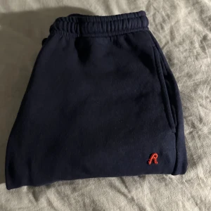 Mörkblå mjukisbyxor från Replay - Mörkblå mjukisbyxor från Replay med elastisk midja och snörning. Byxorna har raka ben, sidofickor och en liten röd Replay-logga broderad framtill. Perfekta för chill dagar eller när du vill vara bekväm men ändå se snygg ut.