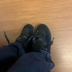 Svarta Uggs lowmel sneakers  - Säljer ett par svarta sneakers med coola mönstrade snören i grått och svart. Skorna har rund tå, platt sula och är tillverkade i syntetmaterial med meshdetaljer för extra komfort. Perfekt för dig som gillar stilrena och sportiga skor.