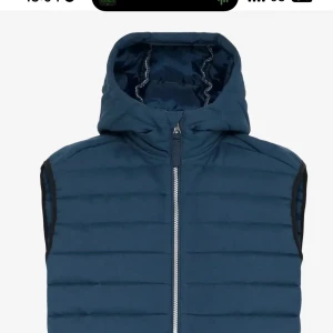 Väst med luva - Snygg mörkblå dunväst med quiltad design och praktisk huva. Västen har en silverfärgad dragkedja framtill och sidofickor med dragkedja. Perfekt att slänga över en hoodie eller tröja för extra värme. Enkel, stilren och passar till streetwear.