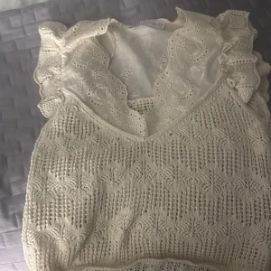 Vit stickad blus med spetsdetaljer - Säljer en vit blus från Zara med stickad framsida och vackra spetsdetaljer vid halsringningen och axlarna. Blusen har volang vid axlarna och ett romantiskt mönster i stickningen. Perfekt för dig som gillar vintagevibbar och detaljer.