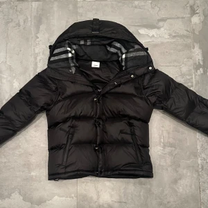 Burberry Vinterjacka  - Säljer min Burberry vinterjacka, storlek M. Jackan är endast använd en gång och är i mycket fint skick.  En varm och elegant vinterjacka i klassisk Burberry-stil, med högkvalitativa material som gör den både bekväm och tidlös. Armarna kan tas av med dragkedja, vilket gör att jackan enkelt kan förvandlas till en väst.  En lyxig vinterjacka för dig som vill ha stil, kvalitet och komfort.                                                                      Billigare vid snabb och smidig affär.
