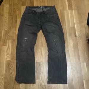Svarta jeans från Original Denim - Svarta jeans från Original Denim med baggy och slitna detaljer på framsidan. Klassisk femficksmodell med knapp och dragkedja. Jeansen har en avslappnad passform och är tillverkade i robust denimtyg.