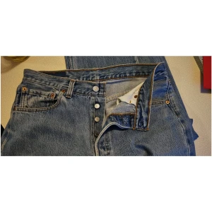 Levi's 501 ljusblå jeans W33 L32 - Klassiska Levi's 501 jeans i ljusblå denim med raka ben och knappgylf. Snygga kontrastsömmar, femficksmodell och ikonisk läderpatch bak. Perfekta för en avslappnad och tidlös look.