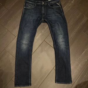 Mörkblå jeans Replay Comfort Fit 33 - Mörkblå jeans från Replay i modellen Comfort Fit, storlek 33. Normal/raka ben passform med snygga slitningar framtill och bakfickor med dekorativa sömmar. 