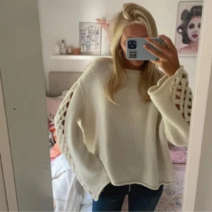 Vit stickad tröja med snörning - Säljer en vit stickad tröja med snygga snörningsdetaljer längs hela ärmarna. Tröjan har en loose passform och långa ärmar med breda muddar. Perfekt för dig som gillar en chill och trendig look med lite extra detaljer.