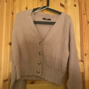 Rosa  ribbad kofta från Bik Bok - Mysig rosa kofta från Bik Bok med ribbad struktur och fyra snygga knappar framtill. Koftan har v-ringning och långa ärmar, perfekt för lager-på-lager-stil. Passar dig som gillar en enkel men trendig look.