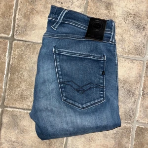 Replay Anbass jeans  - Snygga Replay Anbass hyperflex  jeans i klassisk blå tvätt med diskreta slitningar och raka ben. Modellen har fem fickor. Midja 37cm, längd 104cm. JAG SKICKAR EJ FLER BILDER NÄR JAG BÄR JEANSEN! för storleksguide hänvisar jag till måtten och för bättre inblick i passformen rekommenderar jag att googla på modellnamnet. :) S4