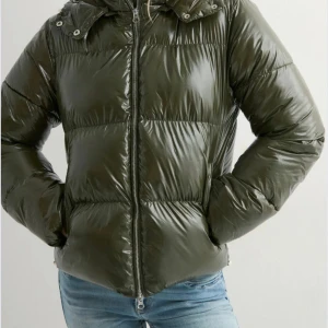 Mörkgrön pufferjacka med huva - Nelly everyday shiny puffer jacket. kommer ej in i lager igen. Snygg mörkgrön pufferjacka med glansig yta och huva. Jackan har dragkedja framtill, två sidofickor och breda, quiltade sektioner som ger en cool look. Perfekt för kalla dagar och enkel att styla med jeans eller mjukis. OBS! fickorna går inte att stänga. går säkert att fixa men nått har hänt så det funkar inte.