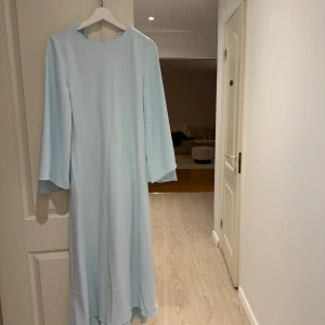 Mango långklänning med vida ärmar - Säljer en stilren ljusblå långklänning med rund halsringning och vida, långa ärmar. Klänningen har en mjuk och flowy siluett som ger en elegant look. Använt 1 gång. Köpt för 1000 kr. 