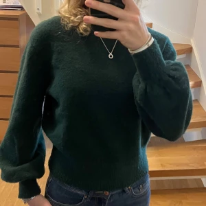 Mörkgrön stickad tröja & Other Stories - Mysig mörkgrön stickad tröja från & Other Stories med ballongärmar och ribbade muddar. Tröjan har en klassisk rund halsringning och är perfekt för lager-på-lager under kyliga dagar.💚