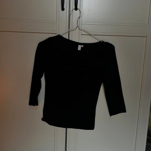 Svart topp med trekvartsärm från Nelly - En stilren svart topp från Nelly i storlek XS. Modellen har trekvartsärm och en rundad halsringning. Toppens passform är figurnära och materialet känns mjukt och stretchigt🌟