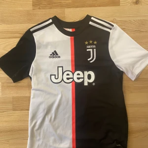 Juventus hemma - Juventus matchtröja från Adidas i storlek L med Ronaldo 7 på ryggen. Tröjan har svart och vit färgblock, röd vertikal linje, korta ärmar och Climalite-material som andas. Juventus-logga med tre stjärnor och Jeep-spons på bröstet. Perfekt för fans av Ronaldo och Juventus. Pris kan diskuteras.