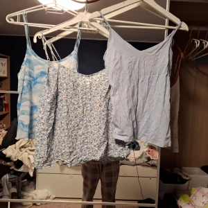 3 somriga linnetoppar i blått och vitt - Säljer tre snygga linnetoppar med smala axelband. En ljusblå från 157 i bomull, en blåvit med molnigt mönster från Monki och en blommig topp från H&M Divided med små blå blommor. Perfekta för varma dagar och chill stil.