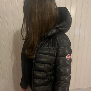 Svart Colmar vinterjacka - Säljer en svart pufferjacka från Colmar i (barnstorlek 12). Jackan har en stor, mysig huva och dragkedja framtill samt två sidofickor med dragkedja. Märket syns tydligt på ärmen med en röd och vit logga. Perfekt för kalla dagar och riktigt snygg stil.