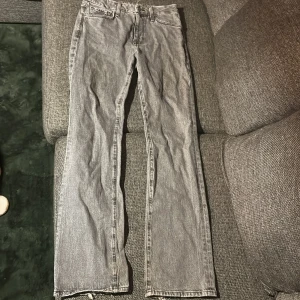 Mid waist jeans - Säljer ett par grå jeans med raka ben, vid hälen är de lite slitna från användning. Jeansen har klassisk femficksdesign och en cool tvättad look. Perfekta för dig som gillar en avslappnad och trendig stil.
