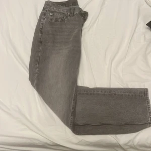 Grå raka jeans från 157 - Snygga grå jeans från 157 med klassisk femficksmodell och raka ben. Jeansen har en något tvättad look och knäppning med knappar framtill. Perfekta för dig som gillar en enkel och stilren vibe.