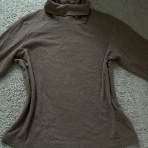 Brun polotröja i mjuk bomull - Enkel och stilren brun polotröja med lång ärm och hög krage. Tröjan är i mjuk bomull och har en normal passform, perfekt för lager-på-lager under kyliga dagar.