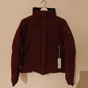 Sail racing vinterjacka - Snygg vinröd pufferjacka från Sail Racing med hög krage och svarta detaljer. Jackan har dragkedjor på fickorna och Sail Racing-logga på ärmen. Materialet är syntet och jackan har en clean, modern look som passar perfekt när det är kallt ute. Helt ny med lappar kvar. 