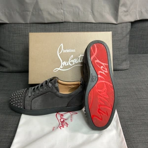 Christian Louboutin grå mocka skor - Snygga grå sneakers från Christian Louboutin i mocka med ikonisk röd sula och coola nitar på tån. Skorna har rund tå, snörning och platt sula. Perfekt för dig som vill sticka ut med exklusiv design och edgy detaljer. Storlek 42