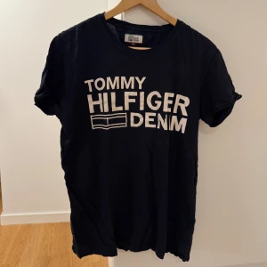 Svart Tommy Hilfiger Denim t-shirt XL - Svart t-shirt från Tommy Hilfiger Denim i storlek XL. Klassisk rund hals och vit tryckt logga framtill. T-shirten har korta ärmar och är gjord i mjuk bomull, perfekt för en chill och stilren look.