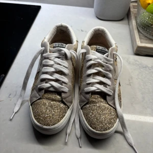 Golden goose skor - Säljer ett par gul glittriga golden goose skor i storlek 8 alltså 40 i svensk storlek, nya skosnören