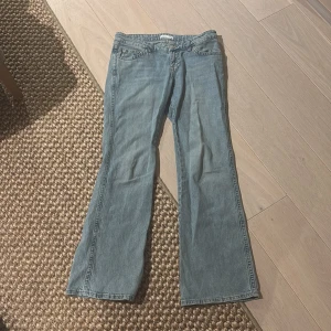 Ljusblå bootcut jeans - Säljer ett par ljusblå bootcut jeans med klassisk femficksdesign och knappgylf. Jeansen har raka ben med lätt utsvängning nedtill och är tillverkade i denim. Perfekta för en avslappnad och trendig look.