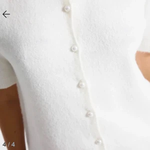 Vit blus med pärlknappar - Superfin vit stickad blus med korta ärmar och rund halsringning. Framsidan har dekorativa pärlknappar som ger en söt och stilren look. Använd ca 2 gånger, därav nytt skick. Orginalpris 125kr🌸