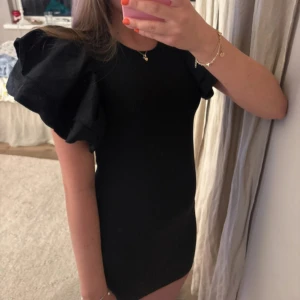 Svart ribbad kortklänning med puffärm - Svart ribbad kortklänning med stora puffärmar som ger en cool och trendig siluett. Klänningen är tight och har en rund halsringning. Materialet är ribbat och känns mjukt mot huden. Perfekt för dig som vill sticka ut med en unik look.