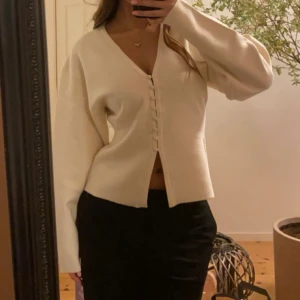 Beige kofta med v-ringning och knappar - Snygg beige kofta med v-ringad hals och dekorativa knappar framtill. Modellen är lite loose fit med långa ärmar och mjukt, stickat material. Perfekt att slänga över en topp för en chill och stilren look.