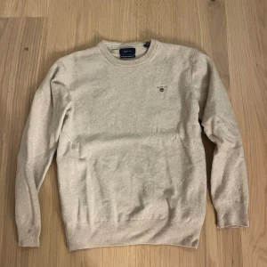 Beige ulltröja från GANT - Beige tröja från GANT i superfin lammull. Den har krympt i tvätten så skulle nog säga att storleken är ungefär 152-158 nått sånt så inte storlek L, den har två hål i armhålorna men går att fixa super lätt, skriv om ni har några funderingar💕