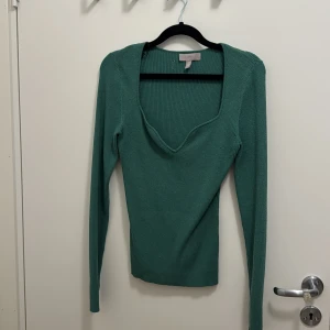 Grön ribbad långärmad tröja H&M - Snygg grön ribbad tröja från H&M med djup v-ringad hals och lång ärm. Modellen är figurnära och har en stilren look som passar perfekt till jeans eller kjol. Materialet är mjukt och stretchigt för en skön passform. Etiketten har lossnat på ena sidan.