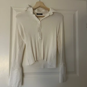 Vit ribbad pikétröja från Praise - Snygg vit pikétröja från Praise med ribbad struktur och klassisk krage. 