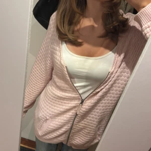 Ljusrosa kofta från Isolde, XL - Supermysig ljusrosa kofta från Isolde i stickat material. Koftanär stickad, har dragkedja framtill och två fickor. Perfekt att slänga på sig över en t-shirt eller linne. Långärmad och med lagade muddar.